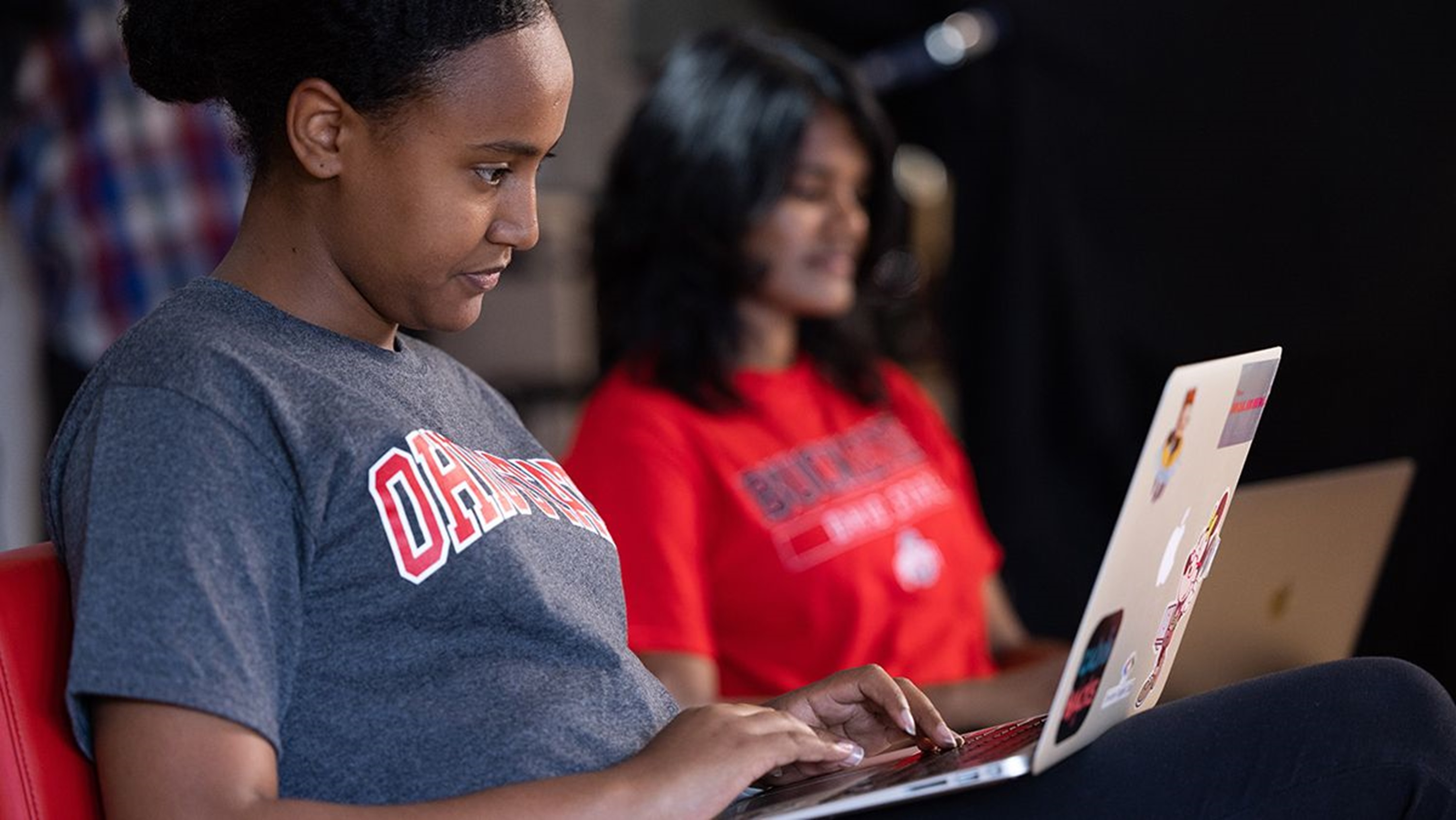 Young woman wearing Ohio State t-shirt working on a laptop.